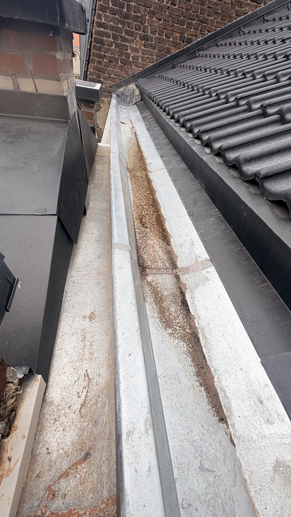 Chéneau en zinc le long d'une toiture en tuiles noires, vu d'en haut